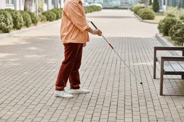 Cropped view of indian blind man in orange vibrant jacket using walking stick while outside — Stock Photo