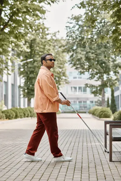 Gut aussehender indischer Blinder mit Brille und Gehstock in orangefarbener Jacke im Park spazieren — Stockfoto