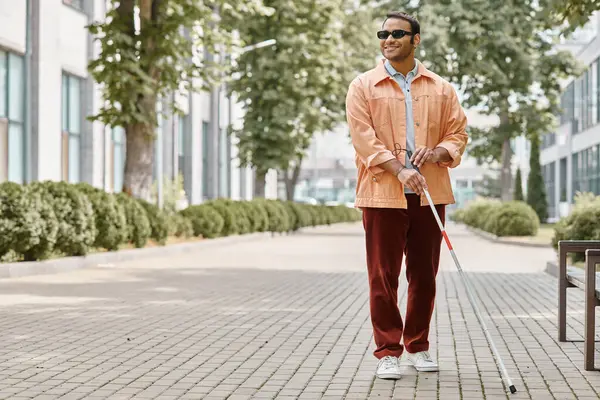 Fröhlicher indischer Blinder mit Brille und Gehstock in orangefarbener Jacke, der im Park spaziert — Stockfoto
