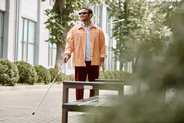 Merry indian blind man with glasses and walking stick in vivid orange jacket walking in park — Stock Photo