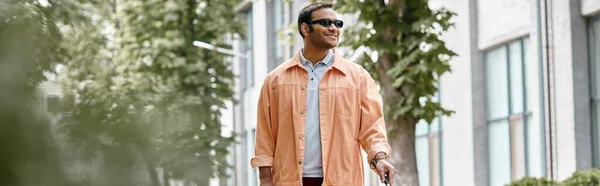 Homme aveugle indien joyeux avec des lunettes et bâton de marche en veste orange vif marche dans le parc, bannière — Photo de stock