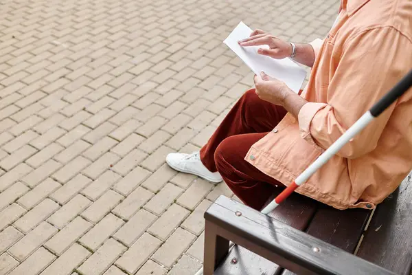 Обрезанный вид индийского слепого человека в оранжевой куртке, сидящего на скамейке и читающего код Брайля — стоковое фото