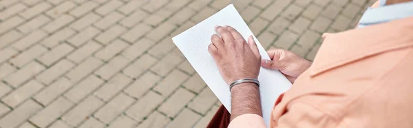 Ausgeschnittene Ansicht eines indischen Mannes mit Blindheit, der auf einer Bank sitzt und Brailleschrift liest, Banner — Stockfoto