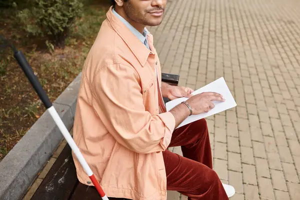 Обрезанный вид индийца со слепотой в оранжевой куртке, сидящего на скамейке и читающего код Брайля — стоковое фото