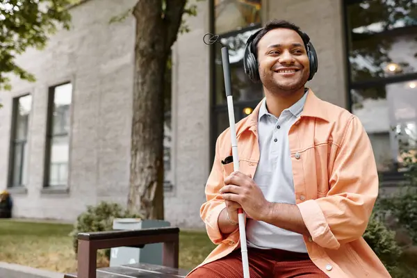 Jolly indian man with blindness in headphones with walking stick enjoying music while outside — Stock Photo