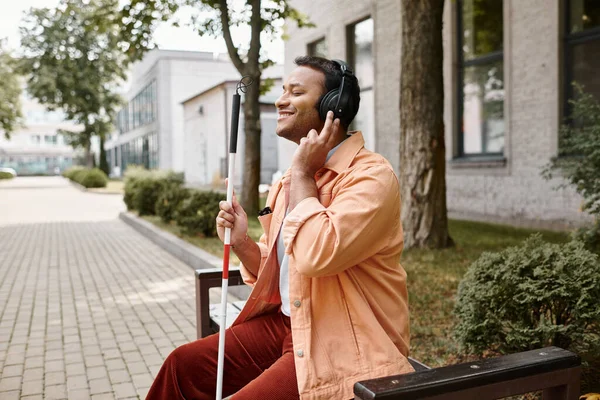 Joyous disabled indian man in casual outfit with headphones and walking stick enjoying music — Stock Photo