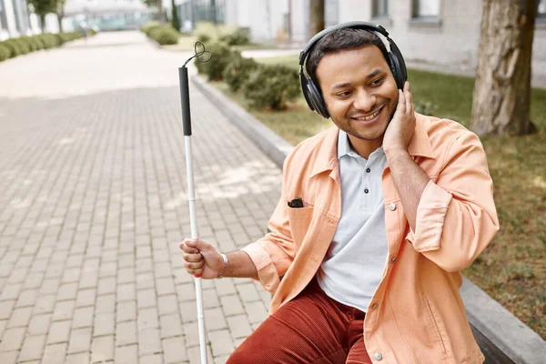 Cheerful disabled indian man in casual outfit with headphones and walking stick enjoying music — Stock Photo