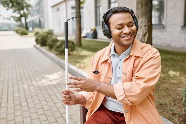 Cheerful disabled indian man in casual attire with headphones and walking stick enjoying music — Stock Photo