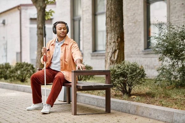 Handsome disabled indian man in casual attire with headphones and walking stick enjoying music — Stock Photo