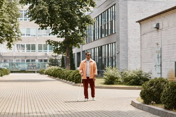 Alegre indio ciego hombre de chaqueta naranja con gafas y bastón caminando caminando en parque - foto de stock