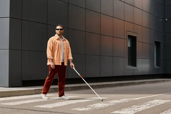 Привлекательный индийский инвалид в оранжевой куртке с очками и палкой с серой стеной на фоне — стоковое фото