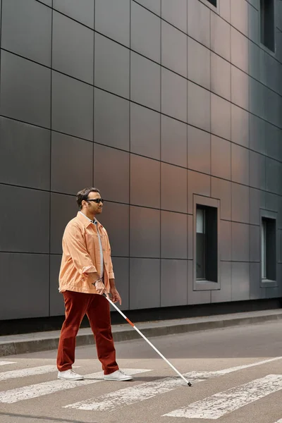 Bonito indiana deficiente homem em jaqueta laranja com óculos e vara com cinza parede no fundo — Fotografia de Stock