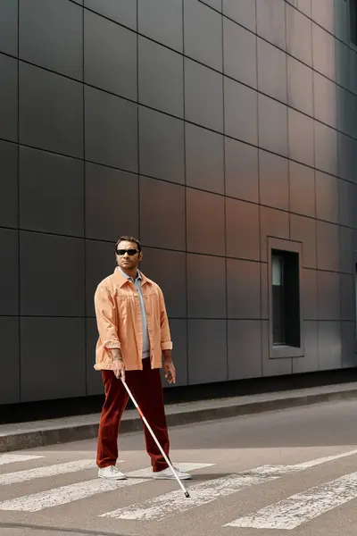 Красивый индийский слепой мужчина в оранжевой куртке в очках и палка с серой стеной на фоне — стоковое фото