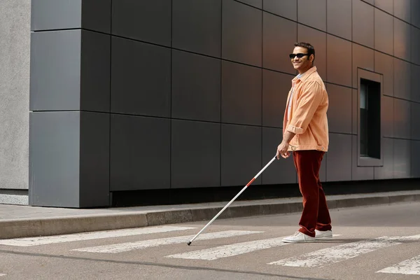 Fröhlicher indischer Blinder in orangefarbener Jacke mit Spazierstock und Brille mit grauer Wand auf Hintergrund — Stockfoto
