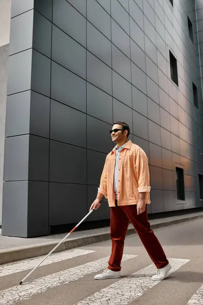 Joyful indian blind man in orange jacket with walking stick and glasses with gray wall on backdrop — Stock Photo