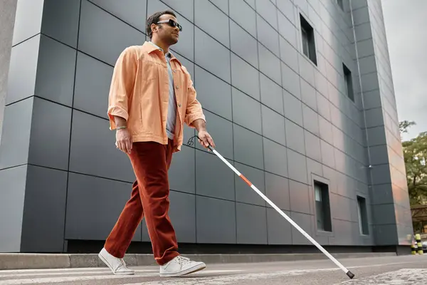 Glad indian blind man in orange jacket with walking stick and glasses with gray wall on backdrop — Stock Photo