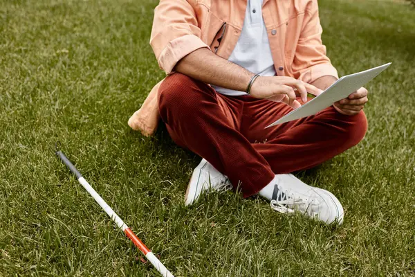 Cropped view of blind indian man in orange jacket sitting on grass and reading braille code — Stock Photo