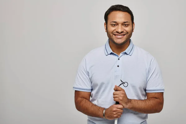 Fröhlicher indischer Behinderter in blauem T-Shirt mit Spazierstock und posiert vor grauem Hintergrund — Stockfoto