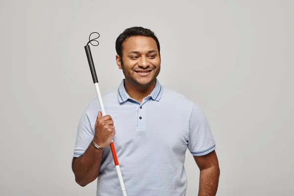 Joyous indian disabled man in blue tee shirt holding walking stick and posing on gray backdrop — Stock Photo