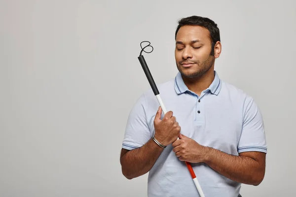 Alegre indio discapacitado hombre en azul camiseta sosteniendo bastón y posando sobre gris telón de fondo - foto de stock