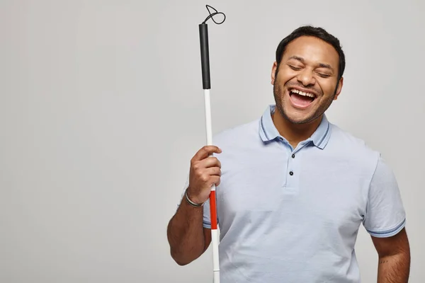 Happy indian disabled man in blue tee shirt holding walking stick and posing on gray backdrop — Stock Photo