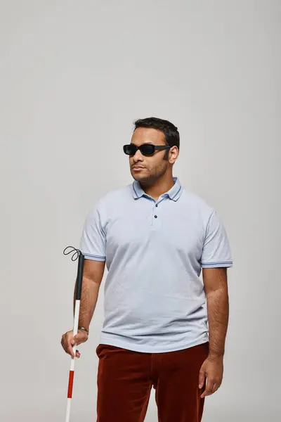 Homem cego indiano de boa aparência em camiseta azul com óculos e vara posando em pano de fundo cinza — Fotografia de Stock