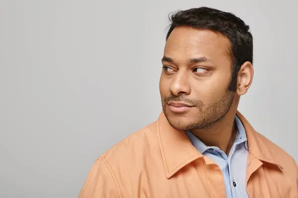 Joyful indian man in vivid orange jacket smiling happily and looking away on gray backdrop — Stock Photo