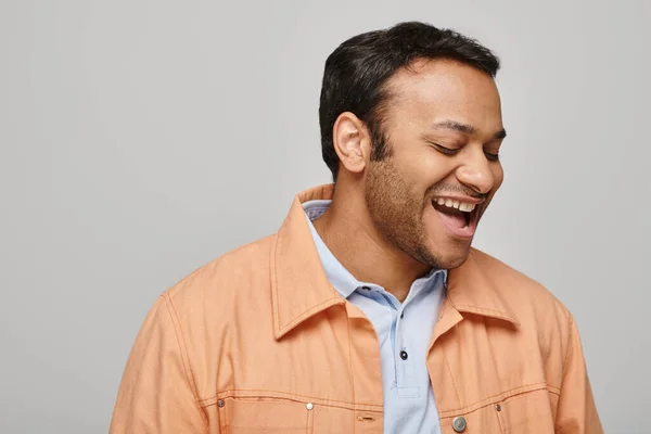 Allegro uomo indiano in giacca arancione vivace sorridente felicemente e guardando lontano sullo sfondo grigio — Foto stock