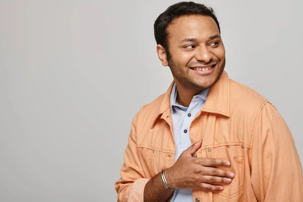 Cheerful indian man in vibrant orange jacket smiling happily and looking away on gray backdrop — Stock Photo