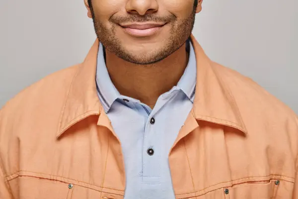 Abgeschnittene Ansicht eines fröhlichen indischen Mannes in orangefarbener Jacke, der vor grauem Hintergrund posiert und glücklich lächelt — Stockfoto