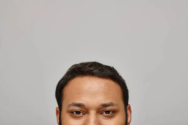 Hübsches indisches männliches Model blickt zufrieden direkt in die Kamera mit grauer Wand auf dem Hintergrund — Stockfoto