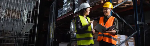 Happy professionals in hard hats talking in a warehouse, middle aged boss and subordinate, banner — Stock Photo