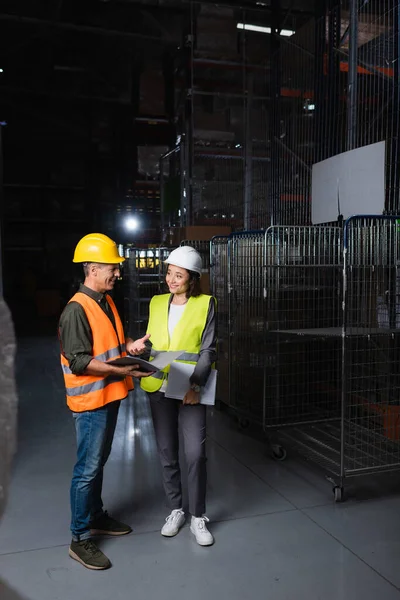Two colleagues with hard hats standing in a well-lit warehouse, supervisor and employee — Stock Photo