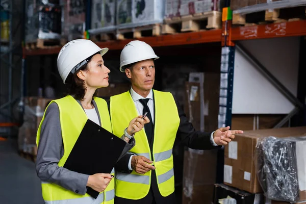 Warehouse supervisor instructing female employee in hard hat and safety vest, inspecting cargo — Stock Photo