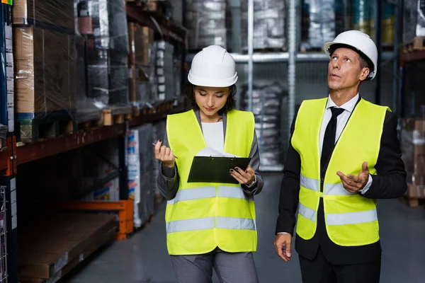 Supervisor discussing productivity of warehouse with female employee in hard hat with clipboard — Stock Photo