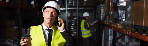 Arbeiter mittleren Alters in Harthut und Sicherheitsweste, der beim Telefonieren einen Kaffee to go in der Hand hält, Banner — Stockfoto