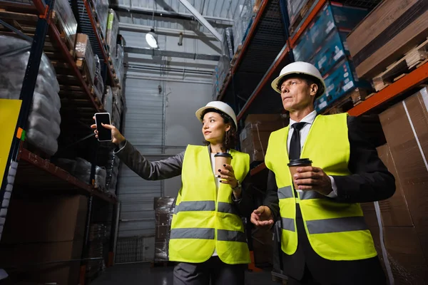 Logistics team, woman in hard hat and coffee showing something to supervisor in warehouse — Stock Photo