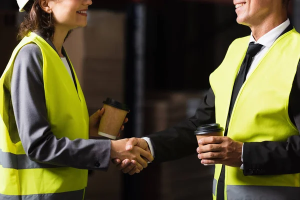 Cropped view of happy supervisor and his colleague holding paper cups with coffee and shaking hands — Stock Photo