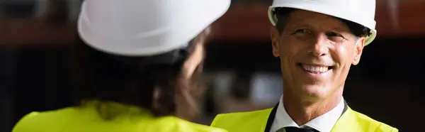 Happy middle aged supervisor looking at female colleague in hard hat on blurred foreground, banner — Stock Photo