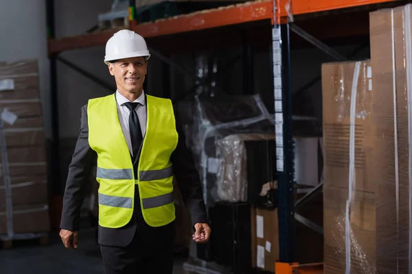 Smiling man in safety vest and hard hat and safety vest walking in warehouse, professional headshot — Stock Photo