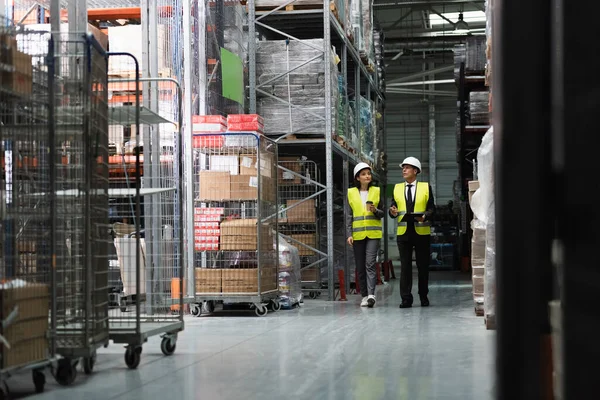 Focused supervisor in safety vest and hard hat inspecting warehouse with clipboard, professional — Stock Photo