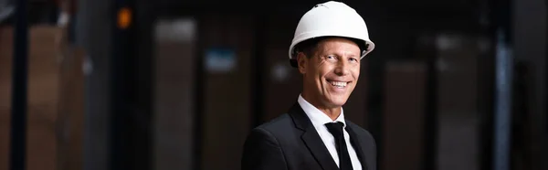 Happy middle aged businessman in hard hat and suit smiling warehouse, professional banner — Stock Photo