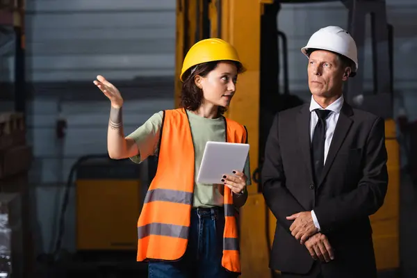 Business meeting in a warehouse, female employee with tablet showing something to supervisor in suit — Stock Photo