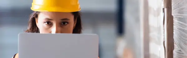 Сфокусированная женщина логистический работник с ноутбуком, глядя на камеру, контроль запасов и грузовой флаг — стоковое фото