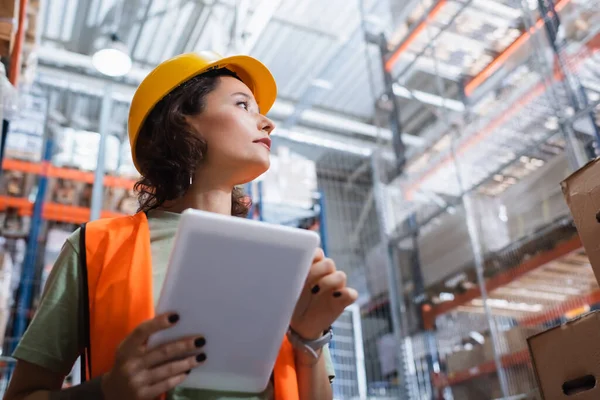 Female warehouse worker in safety vest and hard hat holding digital tablet and checking cargo — Stock Photo