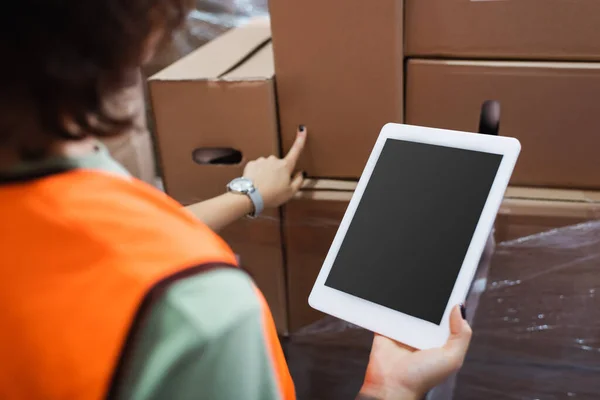 Cropped female warehouse worker in safety vest holding digital tablet and checking cargo — Stock Photo