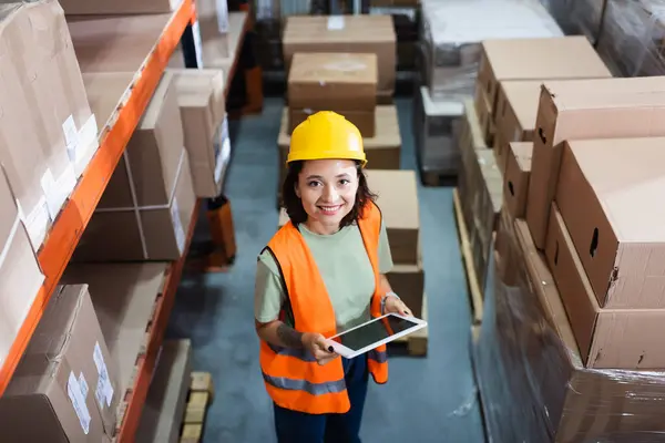 Feliz mujer trabajadora de almacén en chaleco de seguridad y sombrero duro celebración tableta digital, gastos generales - foto de stock