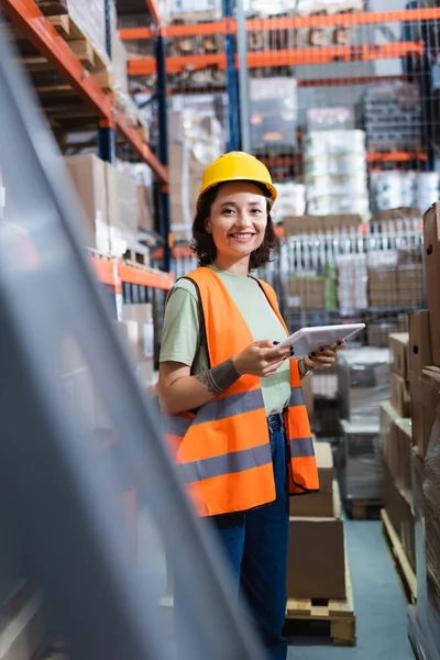 Tattooed happy female warehouse worker in safety vest and hard hat holding digital tablet — Stock Photo