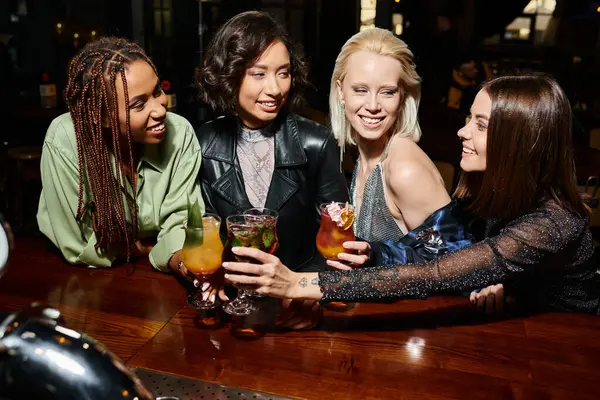 Joyful and stylish multiethnic girlfriends clinking cocktail glasses in bar, modern nightlife — Stock Photo