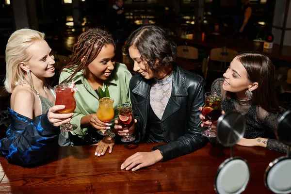 Радісні і модні багаторасові жіночі тости з коктейлями в сучасному нічному барі, дозвілля — стокове фото